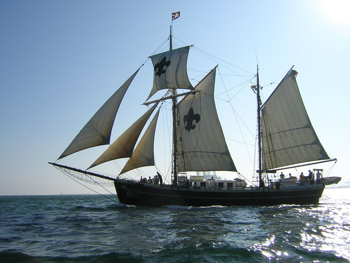 The Argus under full sail, crew on deck, sun low over the water